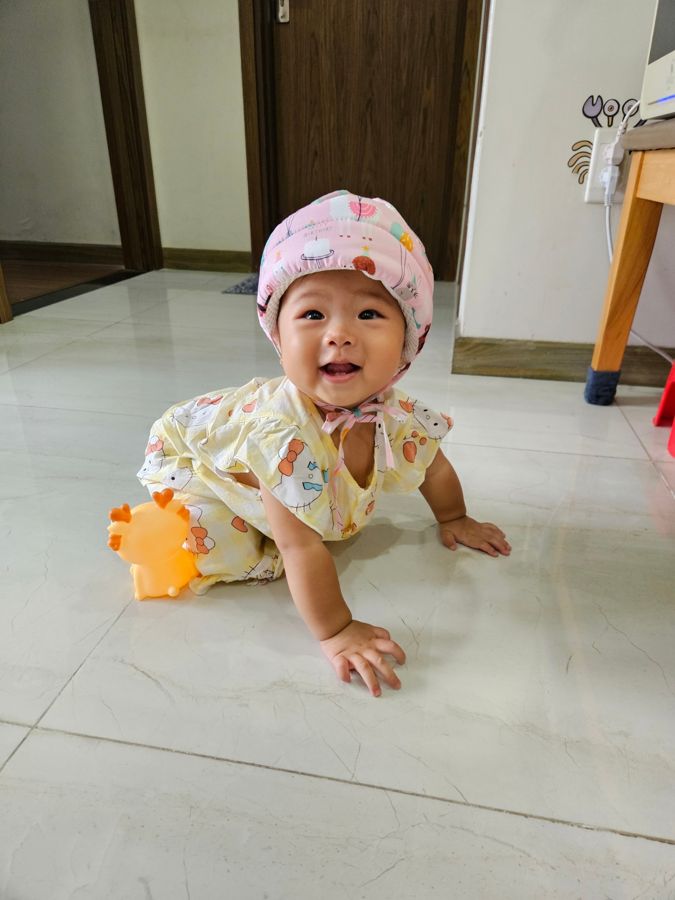 Baby in a pink helmet hat, crawling on the floor and laughing